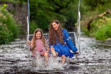 a woman and a young girl are swinging across a fast-flowing river, laughing and splashing with water
