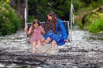 a woman and a young girl are swinging across a fast-flowing river, laughing and splashing with water