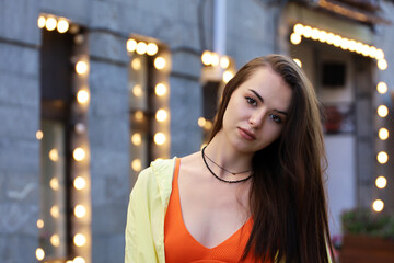 Pretty young girl with long hair and perfect makeup wearing orange top and yellow shirt on a street...