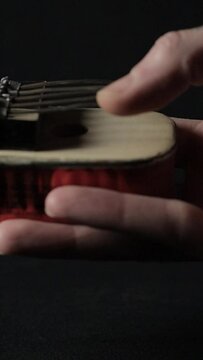 Footage of a hand showing how to play a hand-made Kalimba instrument on a dark background