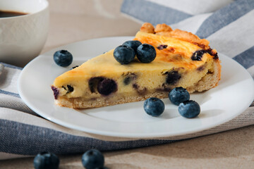 A piece of blueberry cheesecake on a white plate and a cup of coffee on a stone table. Front view