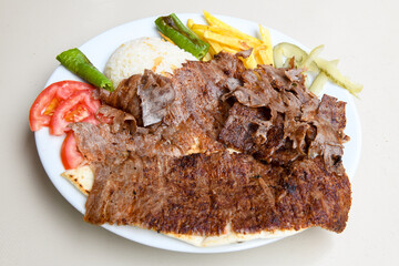 Turkish and Arabic Traditional Ramadan doner kebab with tasty tomato sauce and rice or turkish pilav in white plate on wood table background. ( Pilav ustu doner)