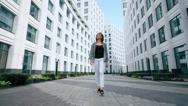 woman is walking in modern business district of big city, full-length moving shot