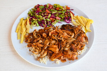Turkish and Arabic Traditional Ramadan chicken doner kebab with tasty tomato sauce and rice or turkish pilav in white plate on wood table background. (Pilav ustu tavuk doner)