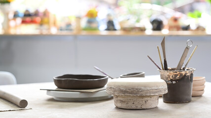 Handmade ceramic dish ware and pottery shaping tools on stone table in creative studio