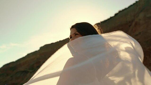  A young girl holds a pareo fabric in the wind overlooking the sea and smiles.