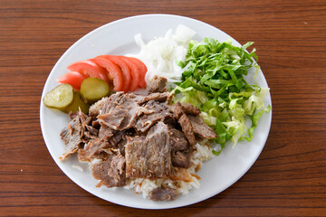 Turkish and Arabic Traditional Ramadan doner kebab with tasty tomato sauce and rice or turkish pilav in white plate on wood table background. ( Pilav ustu doner)