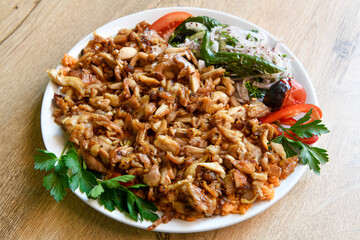 Turkish and Arabic Traditional Ramadan chicken doner kebab with tasty tomato sauce and rice or turkish pilav in white plate on wood table background. (Pilav ustu tavuk doner)