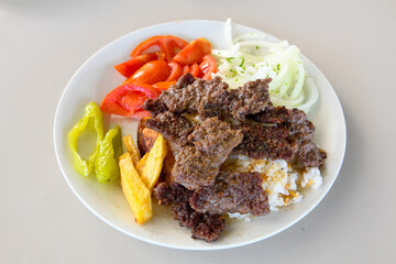 Turkish and Arabic Traditional Ramadan doner kebab with tasty tomato sauce and rice or turkish pilav in white plate on wood table background. ( Pilav ustu doner)