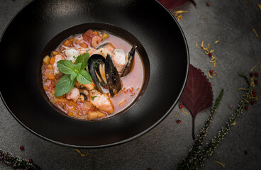 Black round bowl with seafood and vegetables.  Shrimp, mussels, peppermint, heather, leaves.