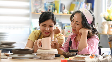 Happy retired woman enjoying hobbies and indoors leisure activity, creating handcrafted ceramics in pottery workshop
