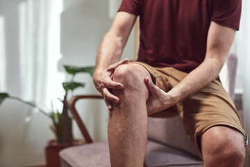 Adult man with knee pain, dislocation, numbness, cramp and other joint issues at home.