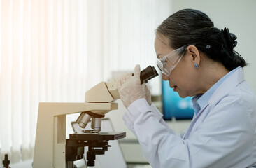 Medical Development Laboratory: Female Scientist Looking Under Microscope, Analyzes Petri Dish Sample. In Background Big Pharmaceutical Lab with Specialists Conducting Medicine, Biotechnology Research