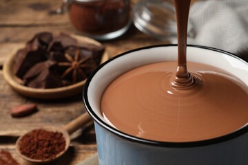Pouring yummy hot chocolate into mug on table, closeup