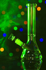 Glass bong with smoke against blurred lights, toned in green. Smoking device