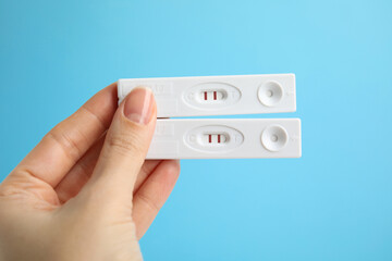 Woman holding two disposable express tests for hepatitis on light blue background, closeup