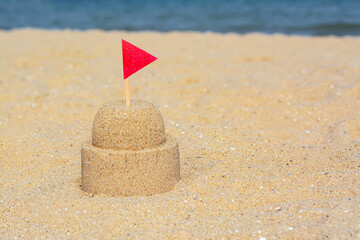 Fototapeta na wymiar Beautiful sand castle with red flag on beach, space for text