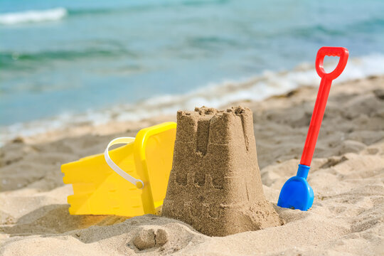 Beautiful sand castle, child plastic shovel and bucket on beach near sea
