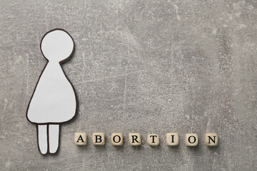 Word Abortion made of wooden cubes and pregnant woman paper cutout on grey background, flat lay....