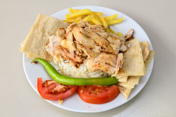 Turkish and Arabic Traditional Ramadan chicken doner kebab with tasty tomato sauce and rice or turkish pilav in white plate on wood table background. (Pilav ustu tavuk doner)