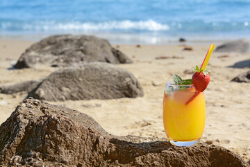 Glass of refreshing drink with strawberry on beach near sea, space for text