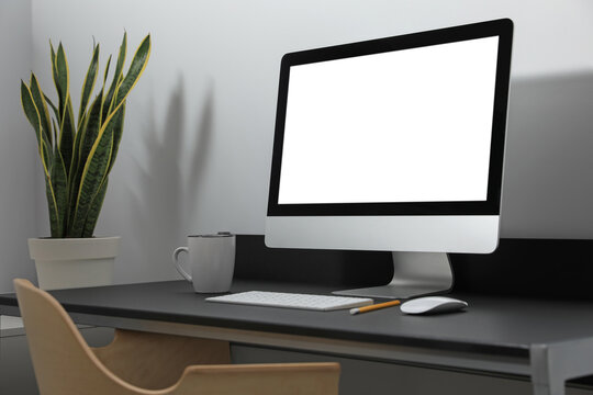 Modern computer with blank screen on black table indoors. Mockup for design