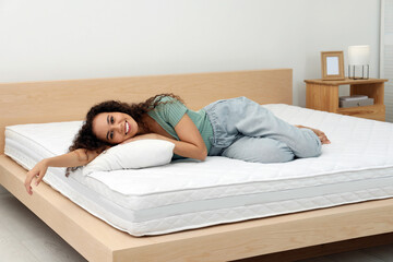 Happy young African American woman on bed with comfortable mattress and pillow at home
