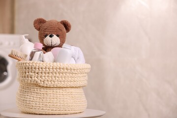 Knitted basket with baby cosmetic products, bath accessories and toy bear on white table indoors....