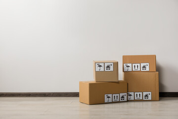 Many closed cardboard boxes with packaging symbols on floor near white wall, space for text. Delivery service
