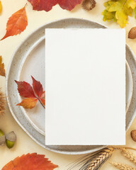 Autumn table place with colorful leaves and vertical blank card top view, mockup