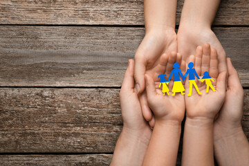 Parents and child holding paper family cutout in colors of Ukrainian flag at wooden table, top...