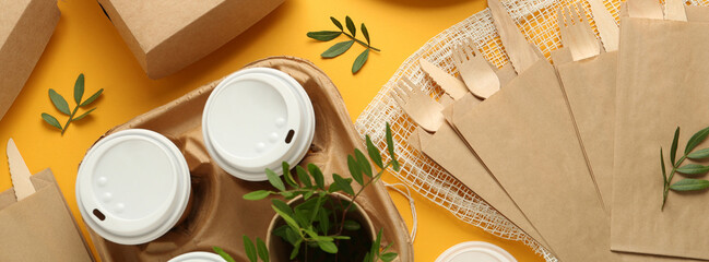 Paper and wooden tableware with green twigs on yellow background, flat lay. Banner design