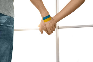 Help for Ukraine. People holding hands with drawing of Ukrainian flag indoors, closeup