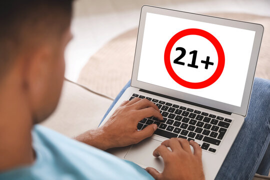 Man using laptop with age limit sign 21+ years indoors, closeup