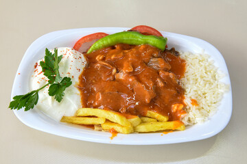 Turkish and Arabic Traditional Ramadan doner kebab with tasty tomato sauce and rice or turkish pilav in white plate on wood table background. ( , Iskender, ekmek arasi pilav ustu doner, doner durum )