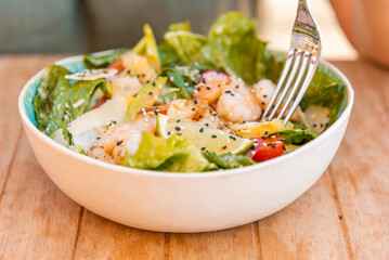 Healthy salad plate. Part woman hand and fork.Fresh summer salad with shrimp, avocado and tomato in bowl on light table. Grilled shrimps and fresh vegetable salad.Healthy food.