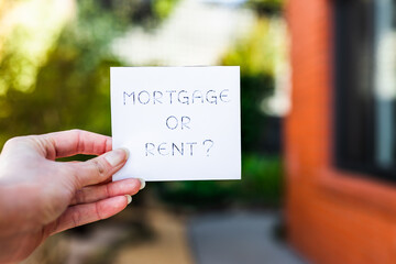 hand holding mortgage or rent sign in front of backyard and home exterior bokeh, real estate affordability and property market