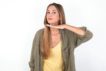 young beautiful woman wearing green overshirt over white background cutting throat with hand as...