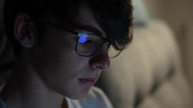 Closeup portrait of cute teenager boy working at night looking at laptop screen, reflected on eyeglasses.