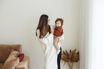 Young mother holds beautiful little daughter in arms. Mother and baby 8 months old play and laugh.