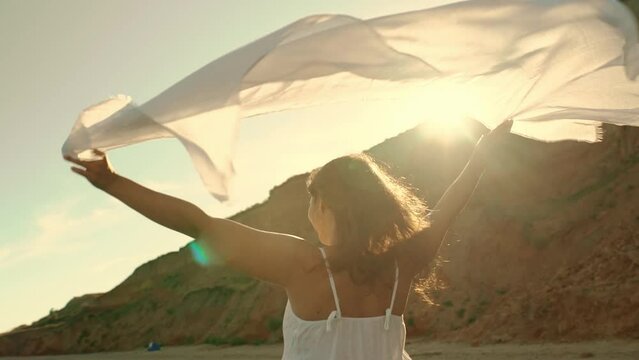  A young girl holds a pareo fabric in the wind overlooking the sea and smiles.