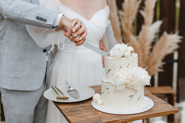 Bride and a groom is cutting their beautiful wedding cake on wedding banquet. Hands cut the cake...