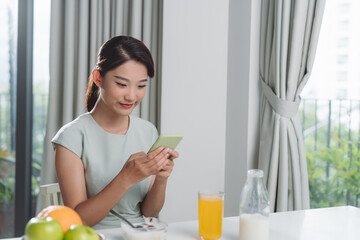 Beautiful cute smiling woman is using smart phone on the kitchen at home. - Powered by Adobe