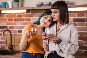 Young cheerful lesbian caucasian couple drinking tea or coffee and enjoying time together at home kitchen. Concept of domestic lifestyle. Idea of homosexual relationship. Spacious apartment. Morning