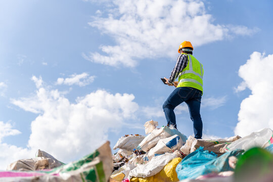 A manager stands holding a tablet on top of the recycling bin at recycling plant. Recycle waste business concept.
