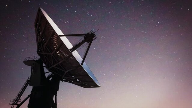 The silhouette of a massive earth-based space observatory satellite telescope scanning the night sky.