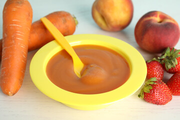 Baby food in bowl and fresh ingredients on white wooden table