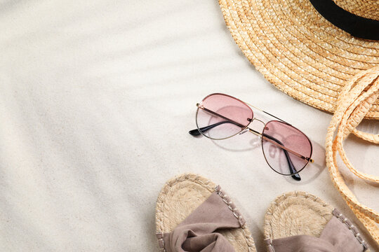 Stylish sunglasses and different beach accessories on sand, flat lay. Space for text