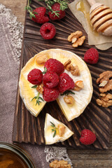 Brie cheese served with raspberries, walnuts and honey on wooden table, flat lay