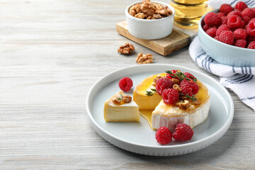 Brie cheese served with raspberries, walnuts and honey on white wooden table. Space for text